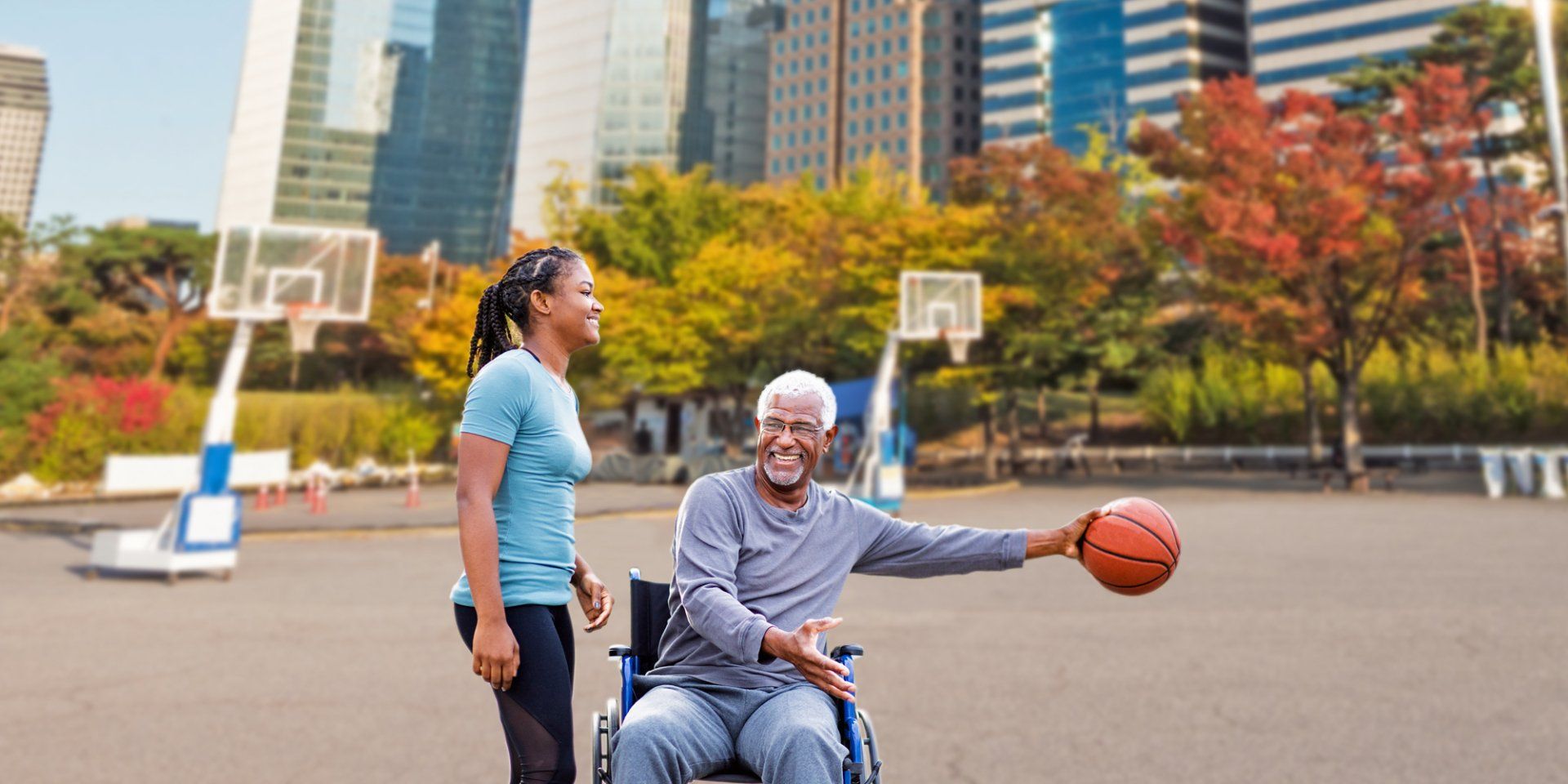 older man in wheelchair holds basketball while younger woman stands next to him