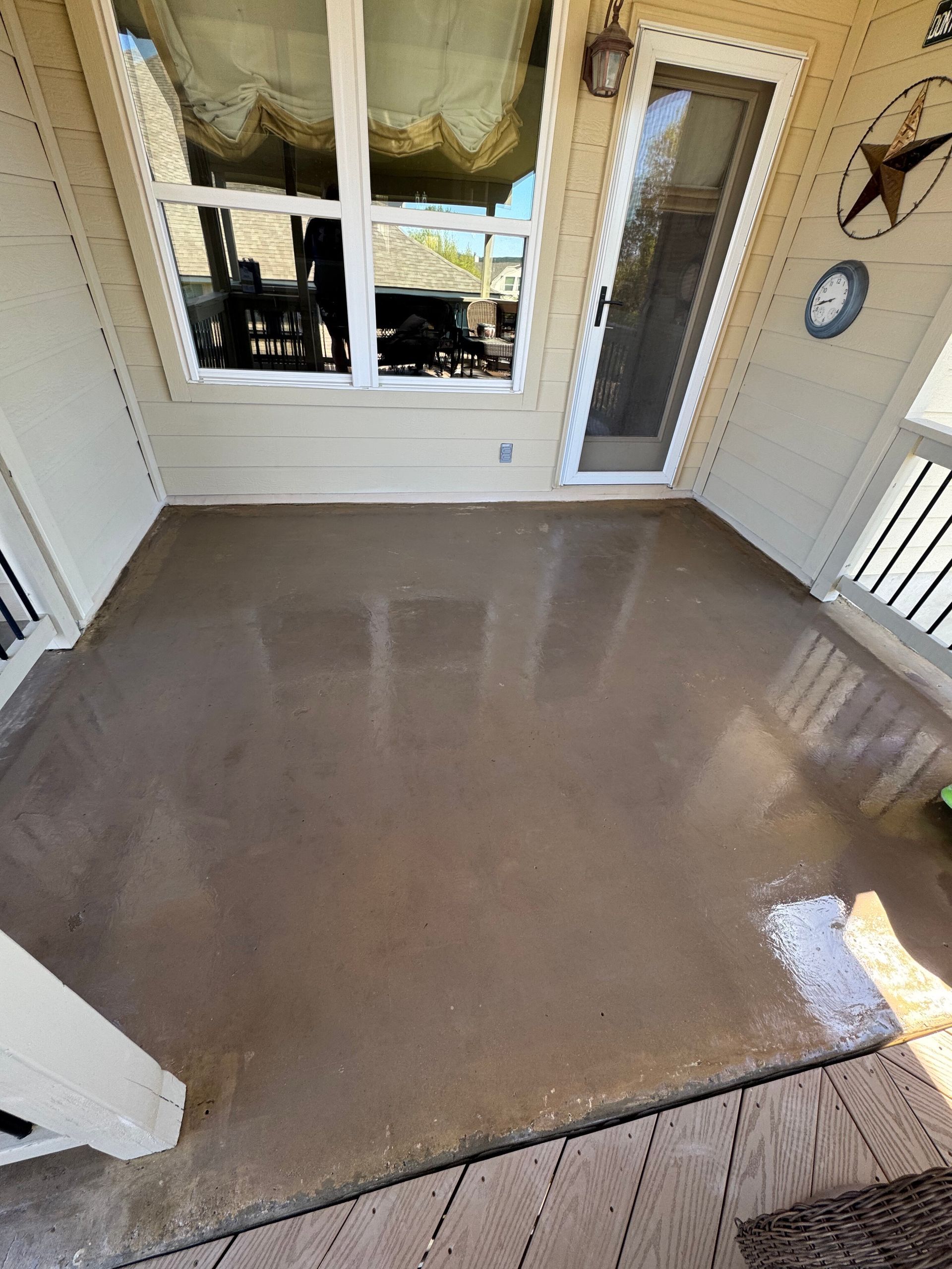 Covered porch with a fresh wet concrete floor, white walls, window, and glass door.