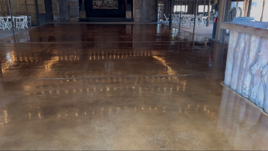 Empty polished wooden floor in a dimly lit indoor hall with benches and tables in the background