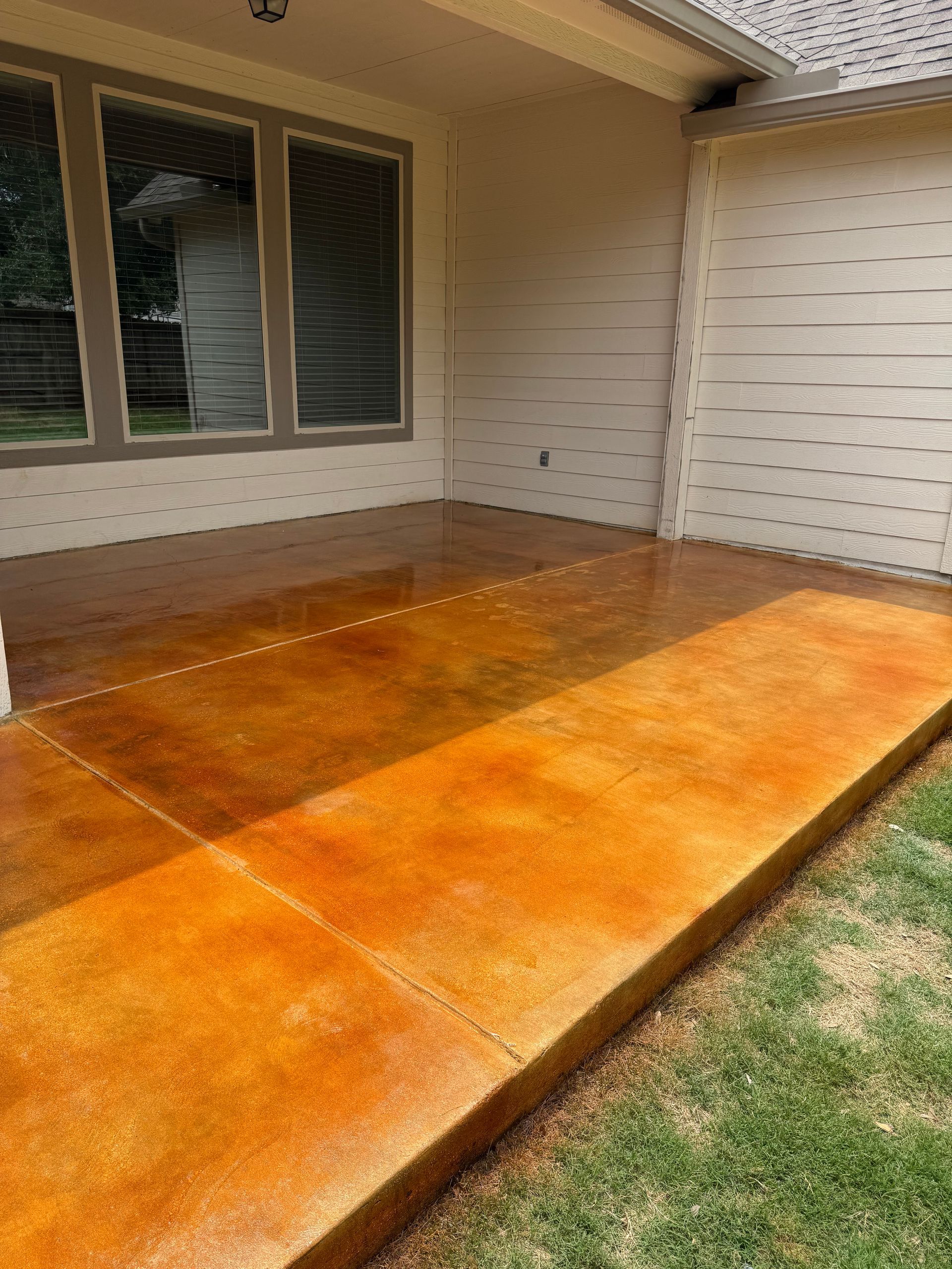 Orange-stained wooden deck beside a house with sliding windows and white siding