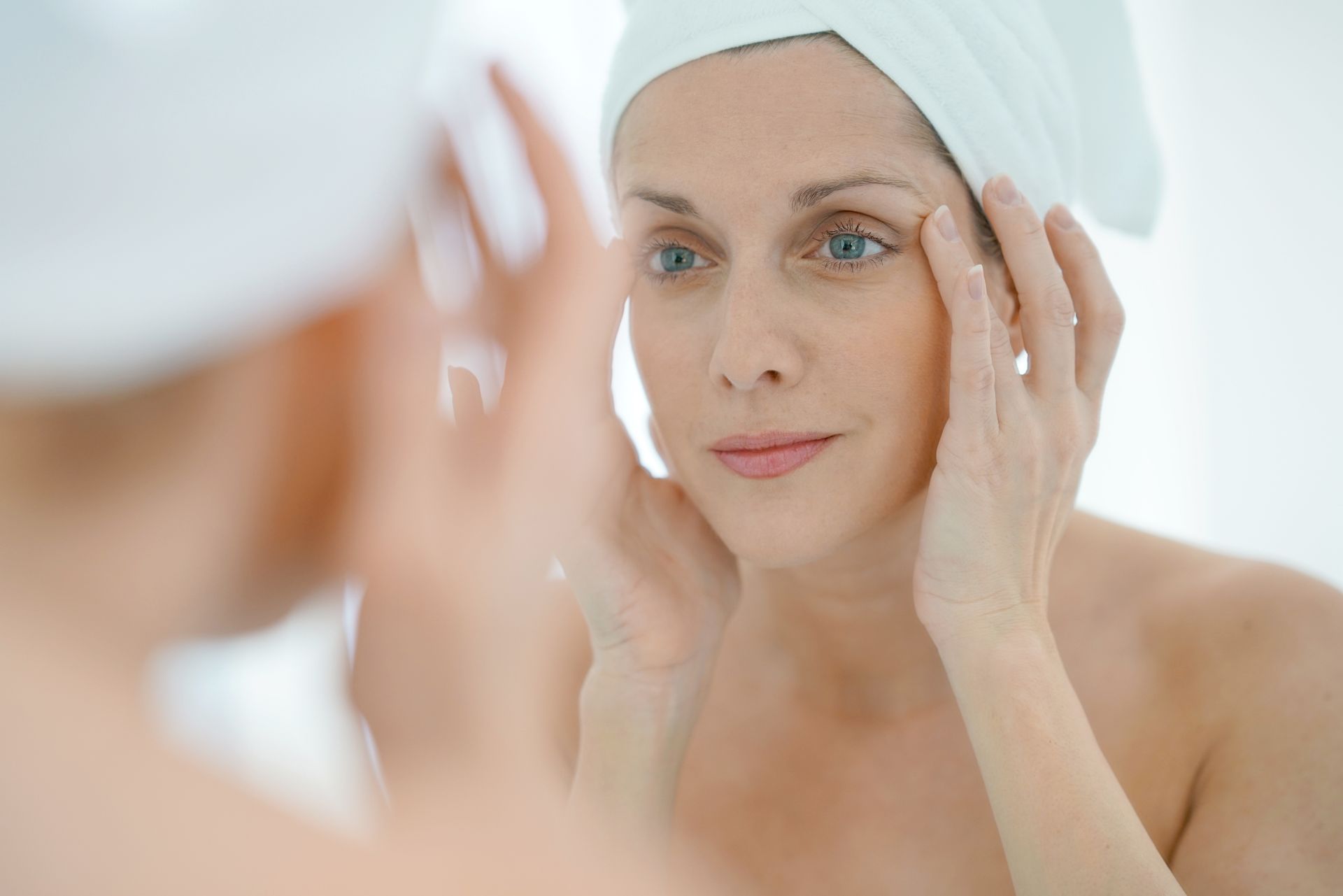 a woman with a towel wrapped around her head is looking at her face in the mirror .