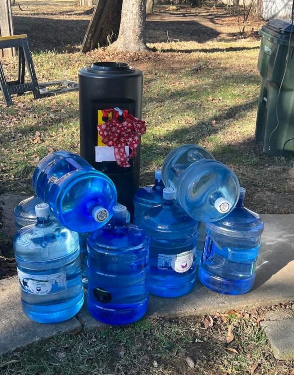 Several blue water jugs and a black water tank outside on grass.