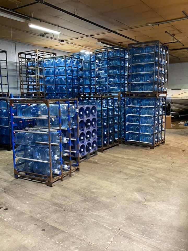 Racks of large, blue water bottles stacked in a warehouse setting.