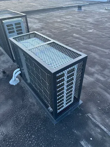 Two rooftop air conditioning units enclosed in black metal cages.