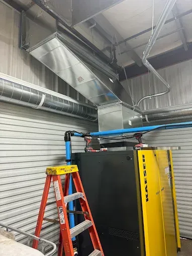 HVAC ductwork and piping installed in a commercial space. A red ladder is next to a large black and yellow machine.