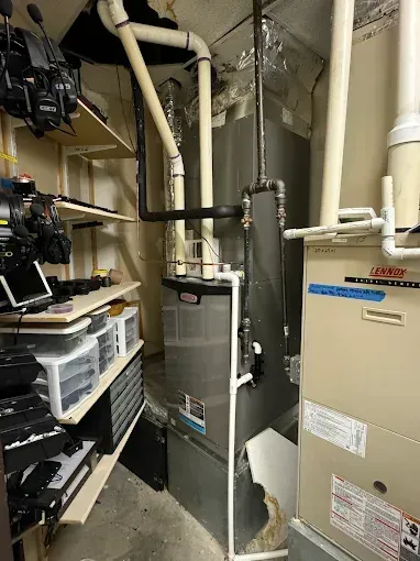 Furnace and water heater in a utility room with storage shelves and ductwork.