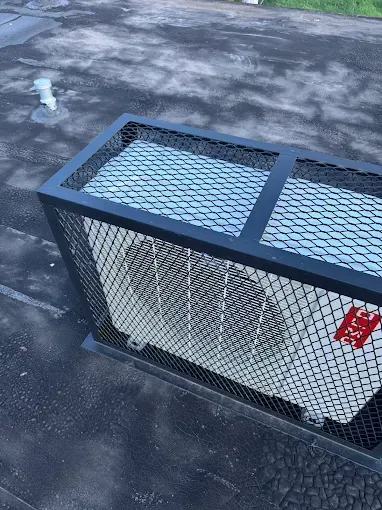 Air conditioning unit on a flat roof, enclosed by a black metal cage.