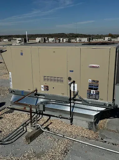 A large rooftop HVAC unit on a building, pipes, and other units in background.