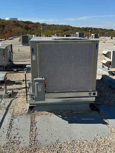 Rooftop air conditioning unit with a large, grey pad, on a flat roof covered in gravel. Blue sky in background.