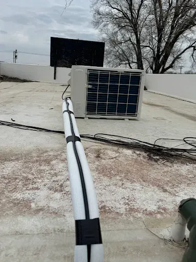 HVAC unit on a rooftop with insulated pipes running across the surface, overcast sky.