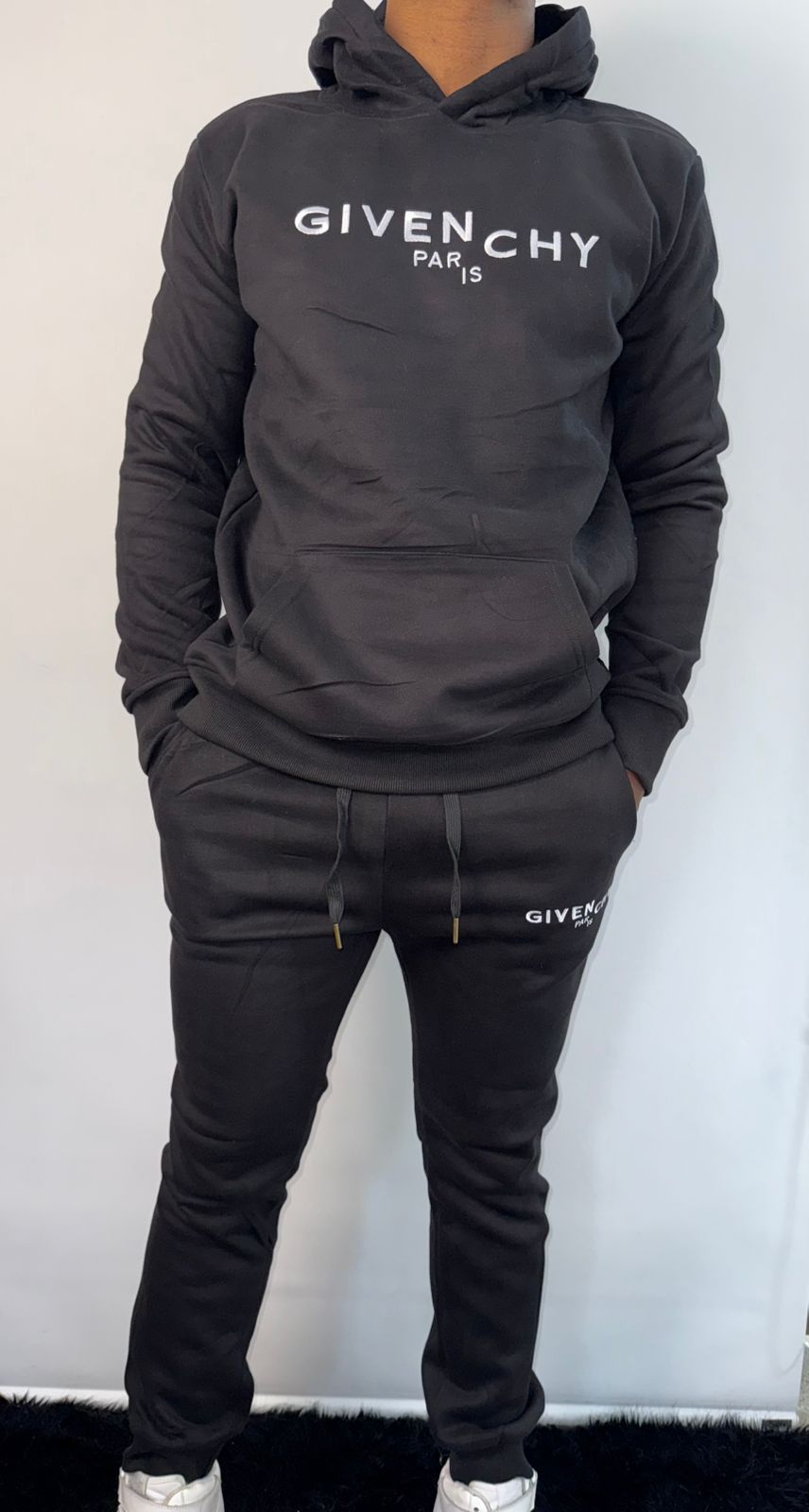 Persona vestida con un chándal negro de Givenchy, de pie con las manos en los bolsillos.