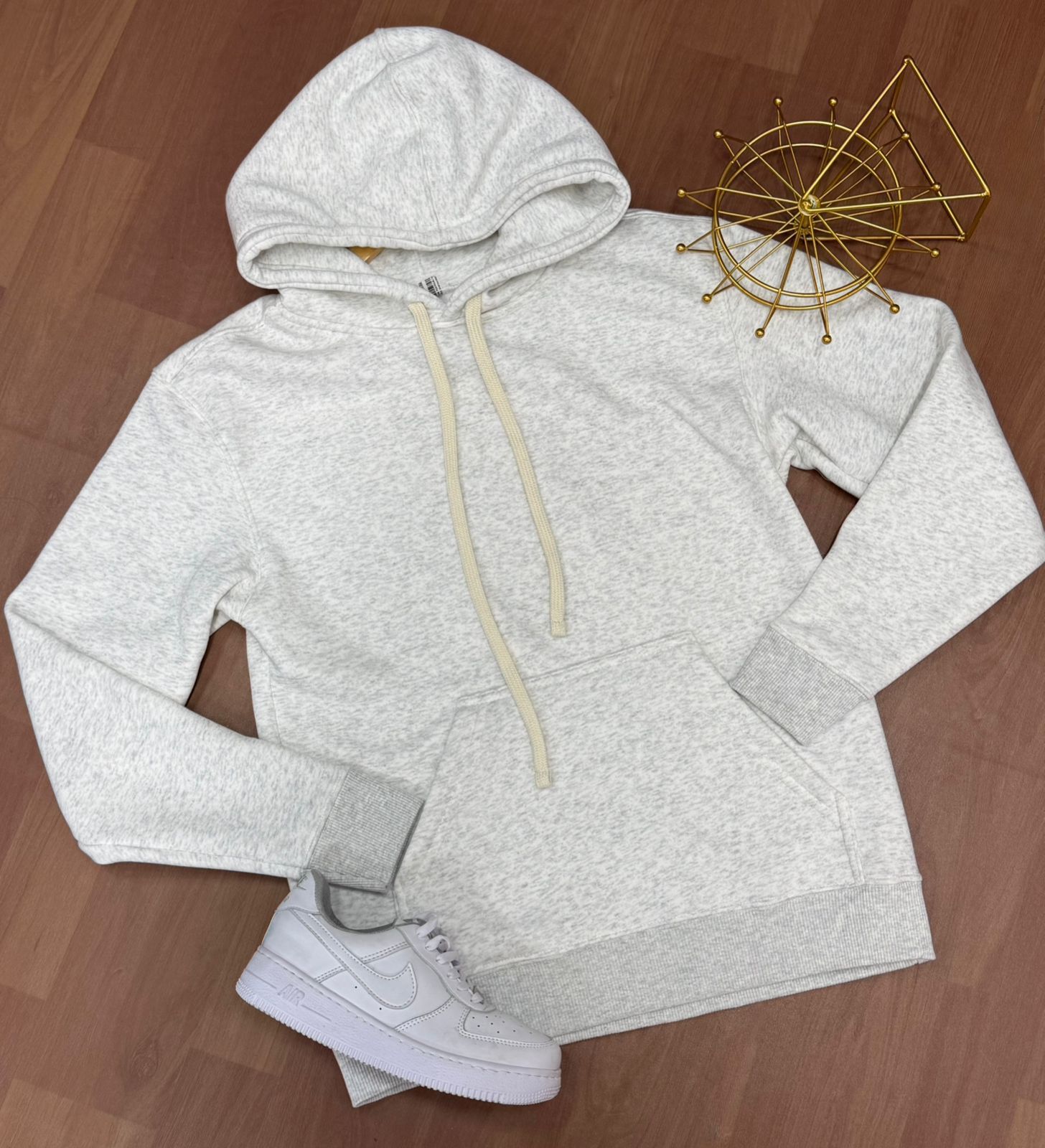 Sudadera con capucha gris claro con cordón color crema y bolsillo delantero, combinada con una zapatilla blanca.