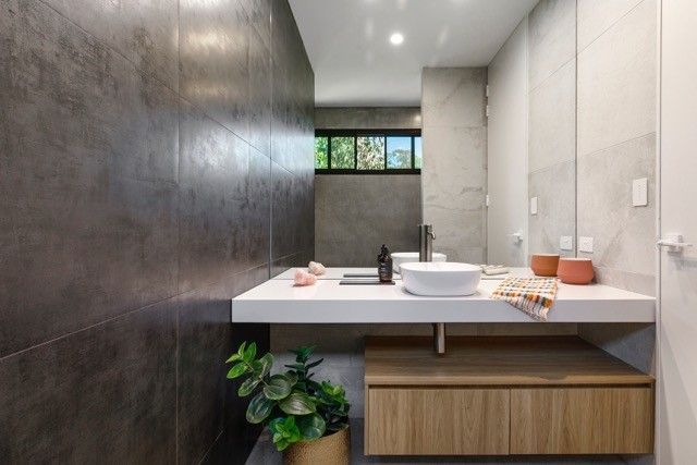 A modern bathroom vanity with a white basin, wooden cabinet, and a large mirror against dark tiled and grey walls. — Foreshore Kitchens in Coolum Beach, QLD