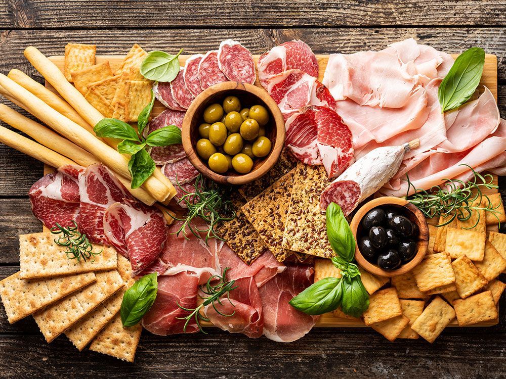 A wooden cutting board topped with a variety of meats and crackers.