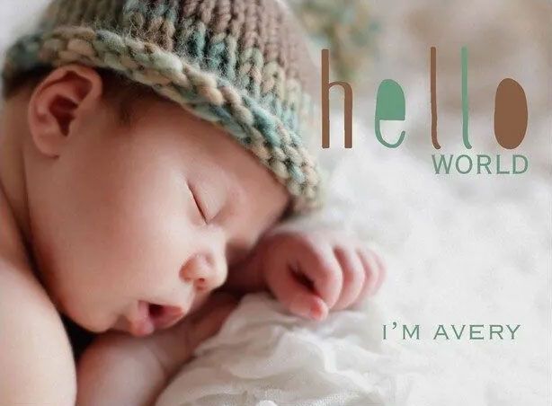 A baby wearing a knitted hat is sleeping on a bed with the words hello world i 'm avery