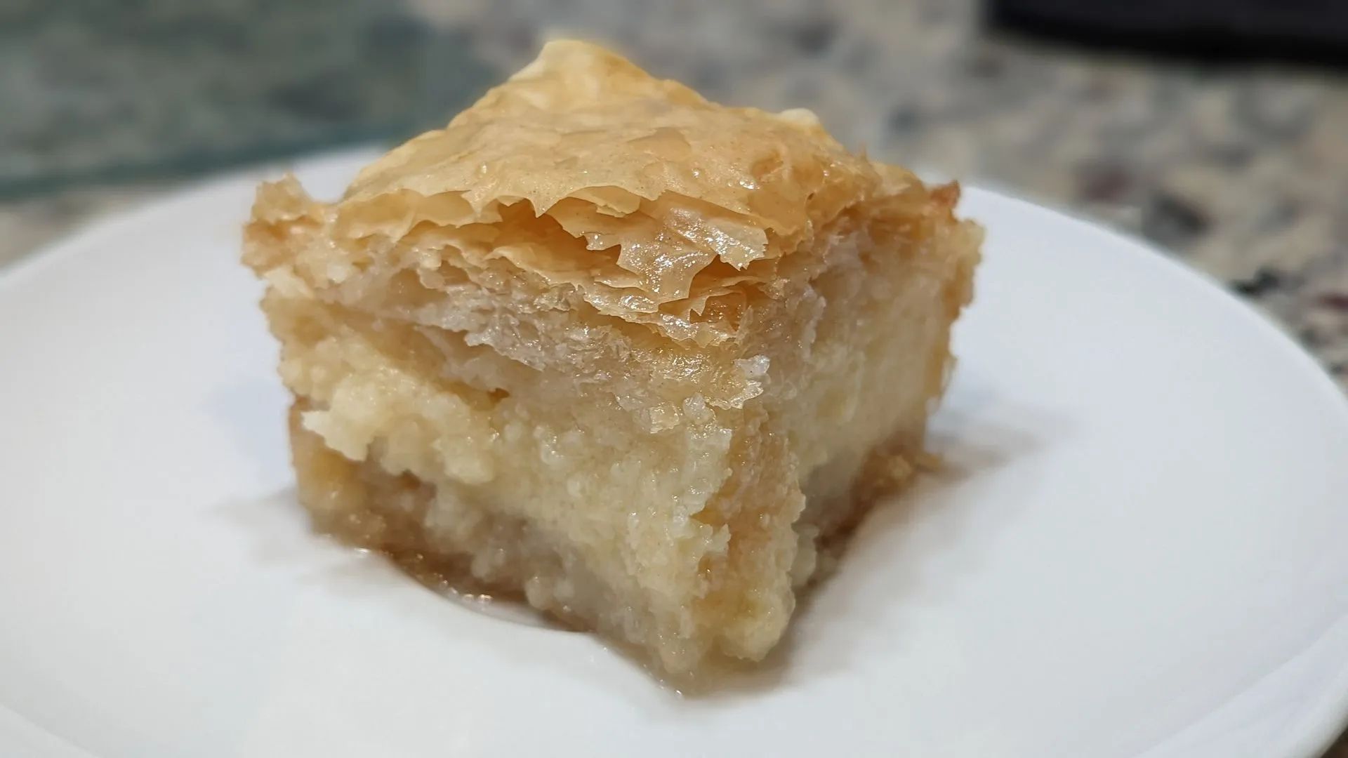 A piece of baklava is on a white plate.
