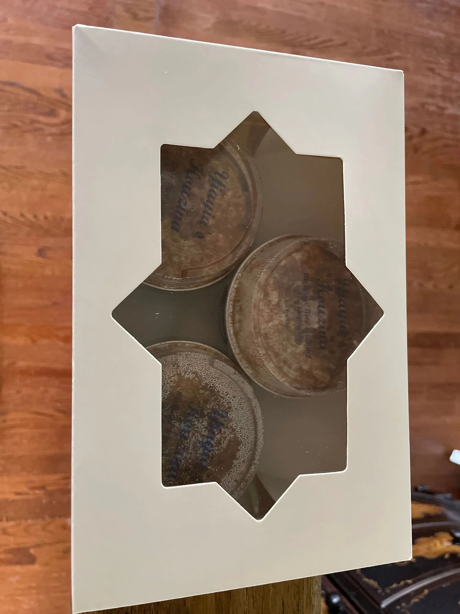 Three cupcakes are in a white box with a window.