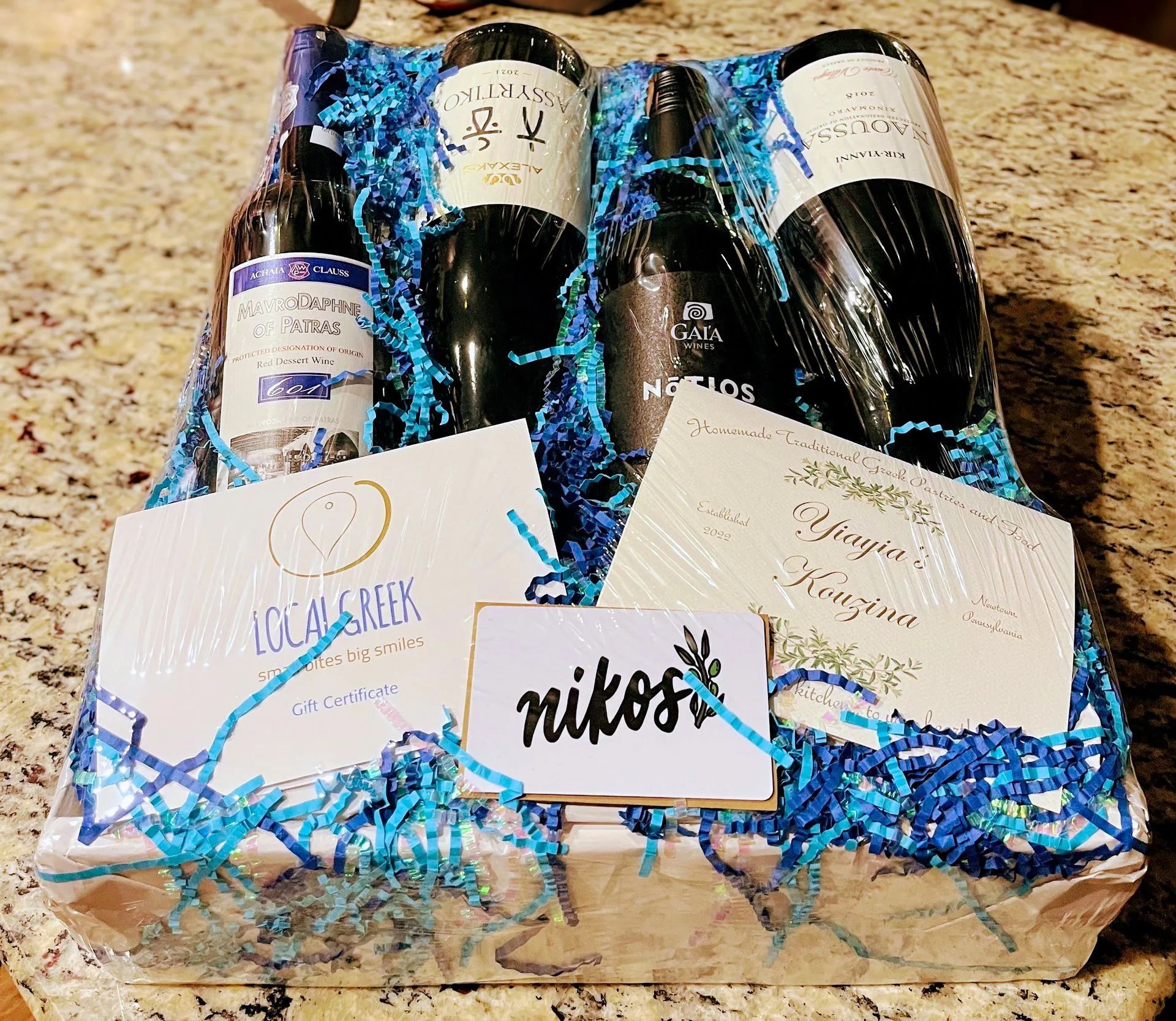A gift basket with three bottles of wine and a card that says nikos