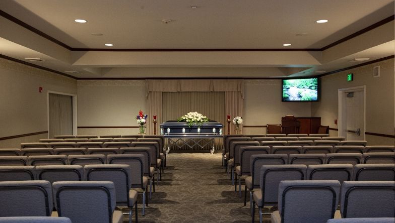 An empty funeral home with rows of chairs and a coffin in the background.