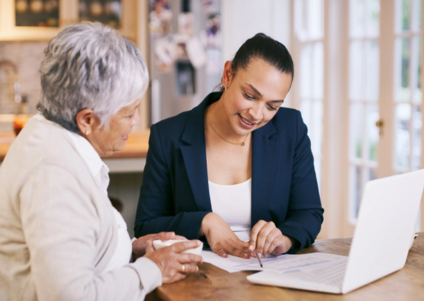 two women are sitting at a table looking at a laptop .