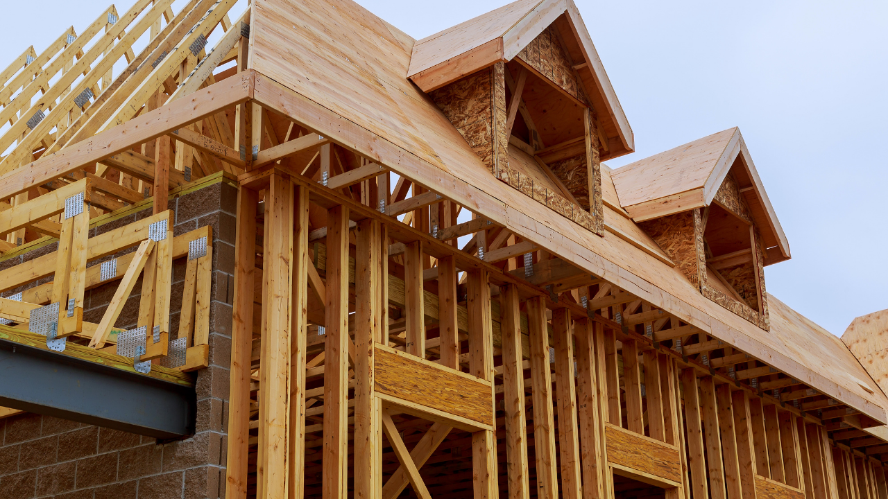 Wooden house under construction; exposed framing, roof rafters, dormers.