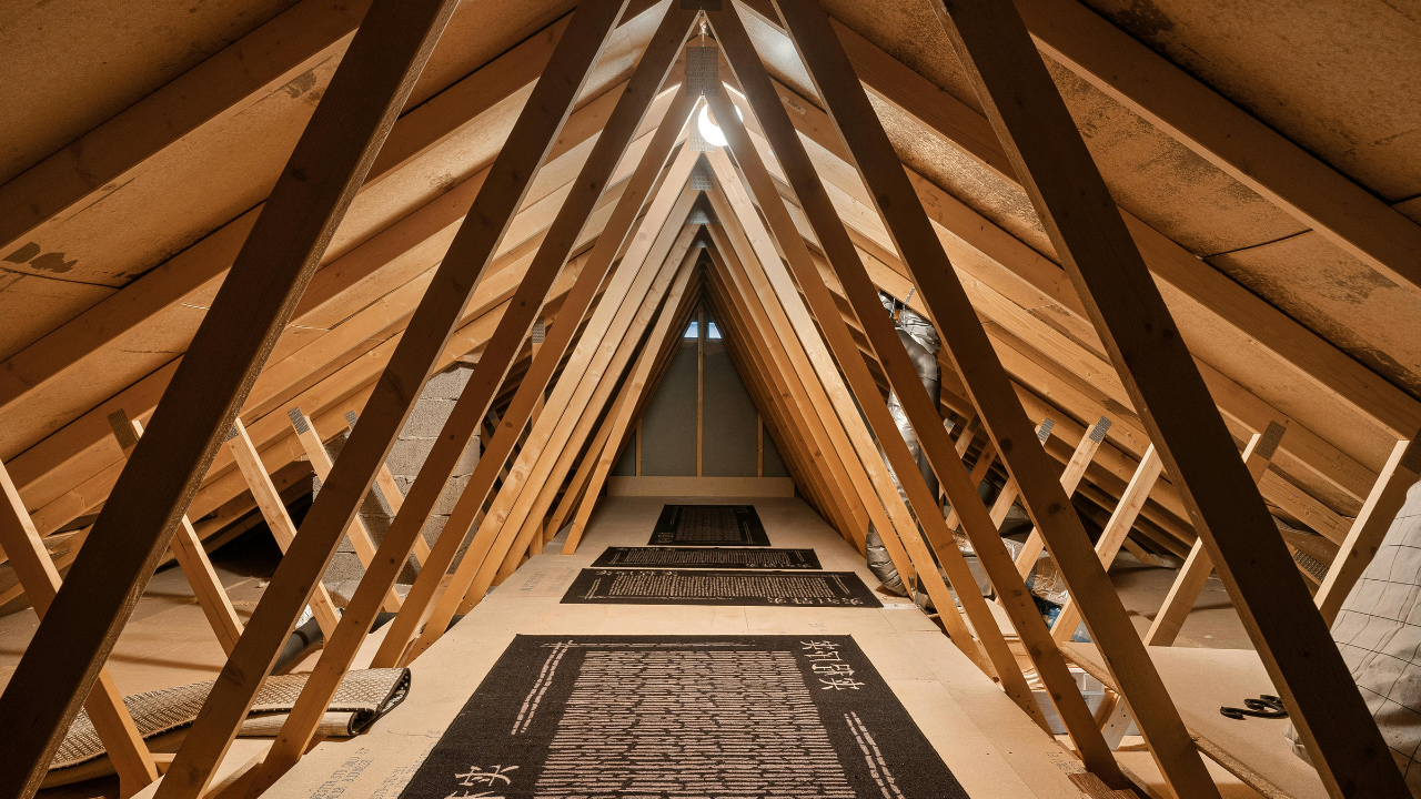Wooden attic rafters converging upwards; rugs on floor below.
