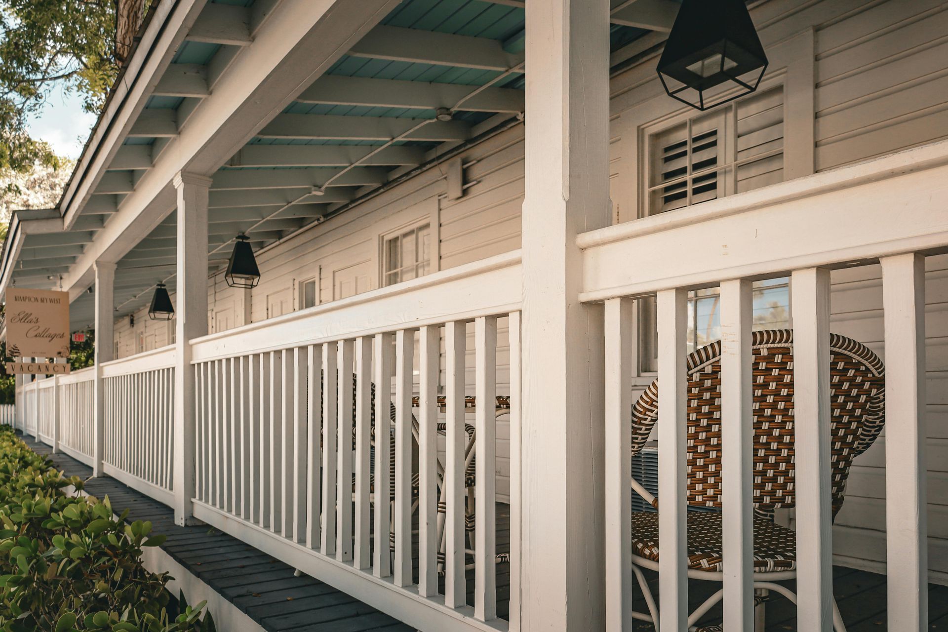 White porch with railing and wicker chair. Building has a blue ceiling.