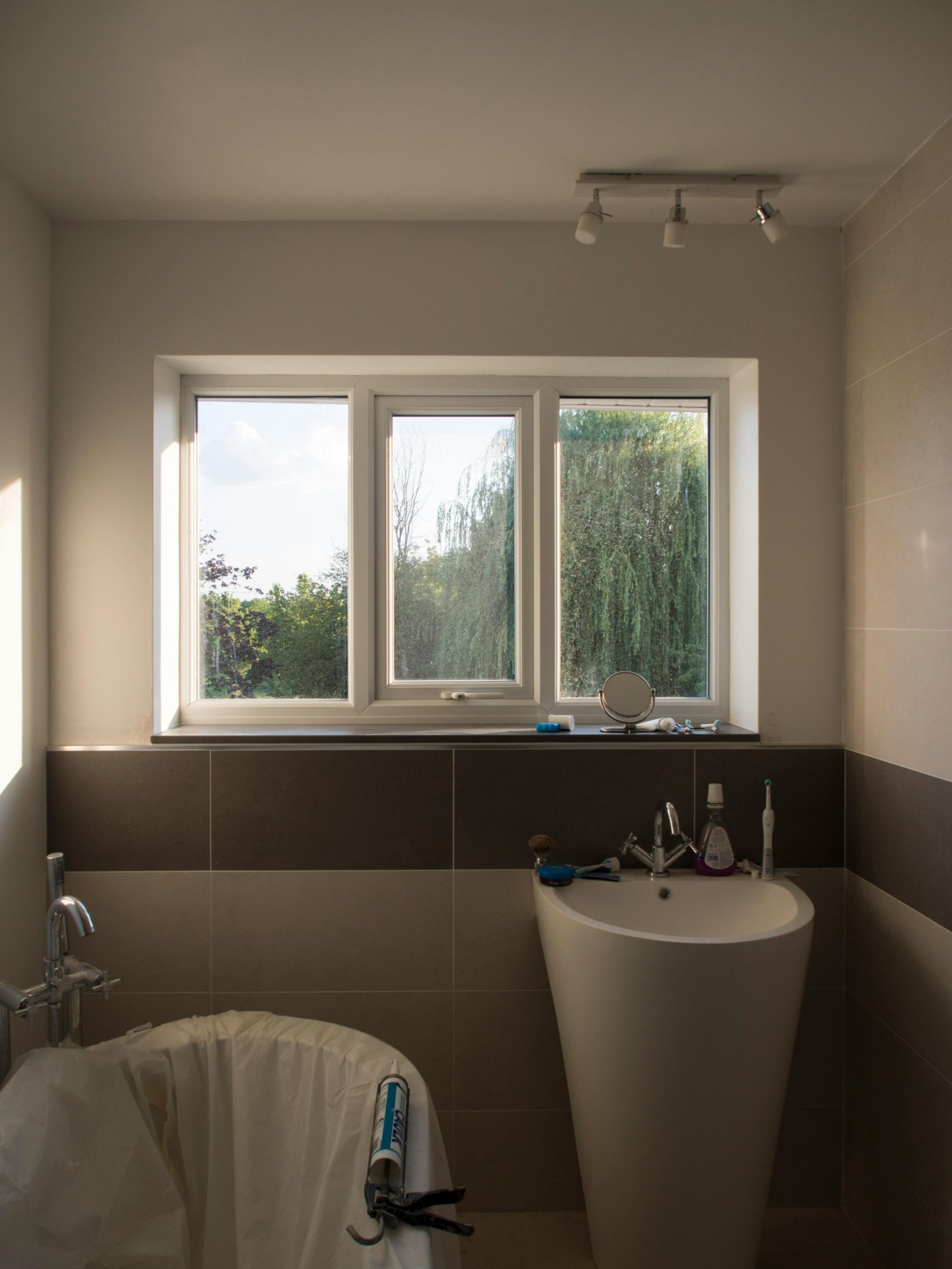 Bathroom with a white sink, window, and brown and beige tile.