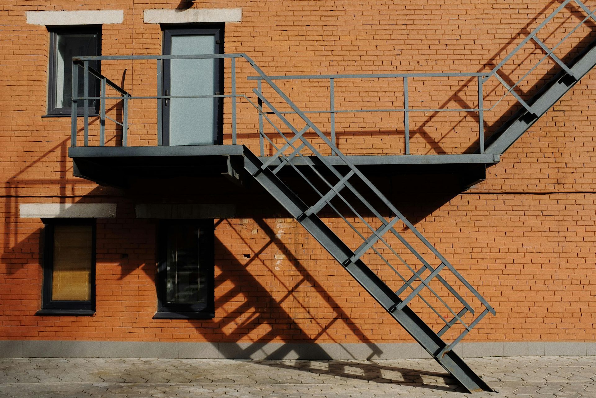 Brick building with metal fire escape stairs and landing casting a shadow.