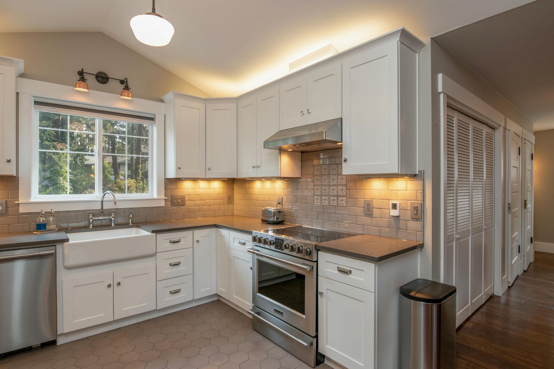White kitchen with stainless steel appliances, grey countertops, and a window.