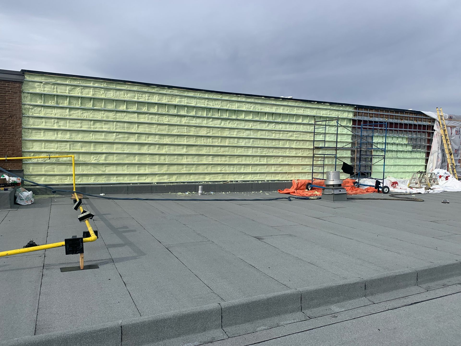 Construction extérieure du bâtiment avec isolation jaune et toiture grise.