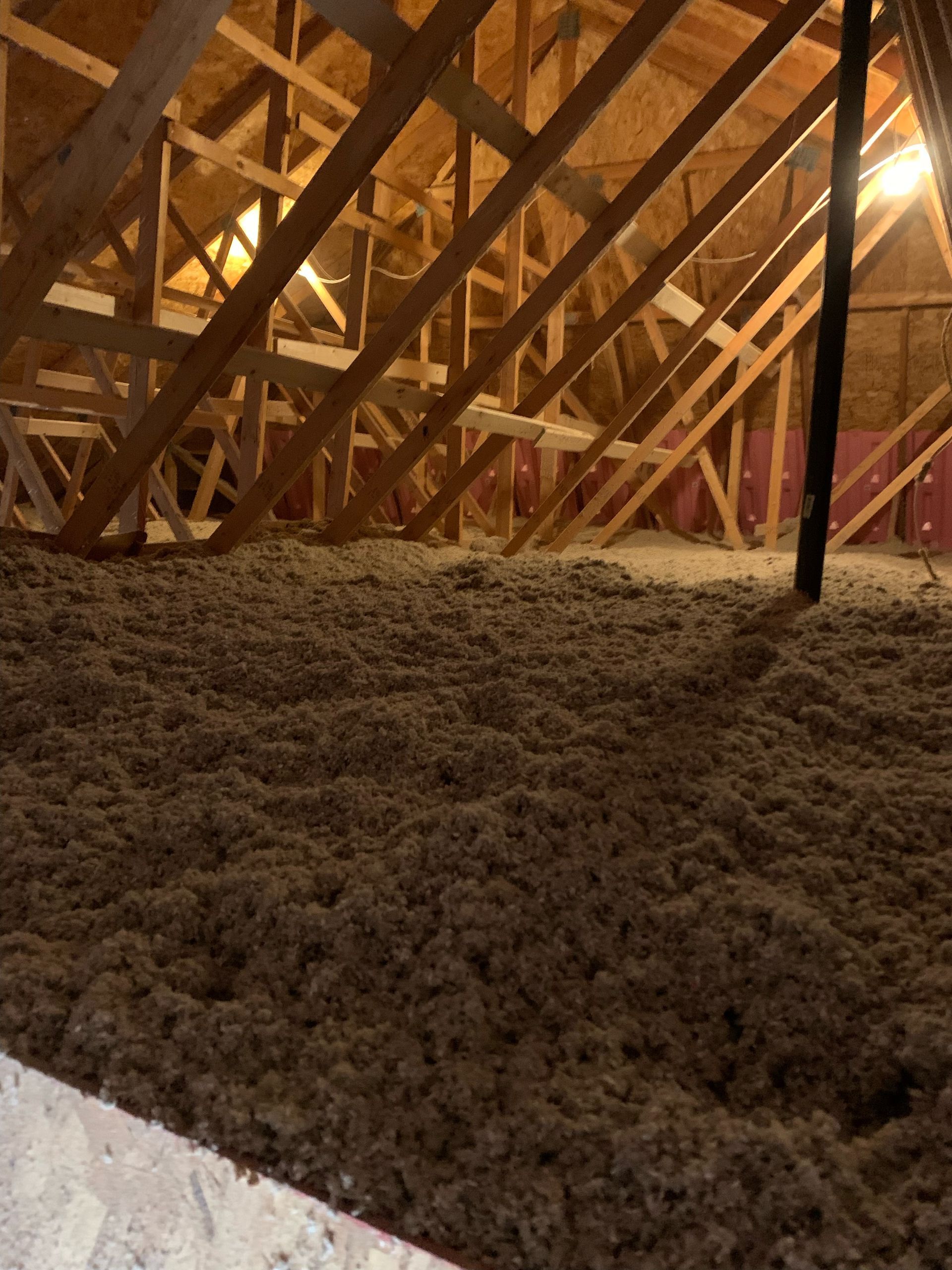 Grenier rempli d'isolant brun ; des chevrons en bois soutiennent le toit.