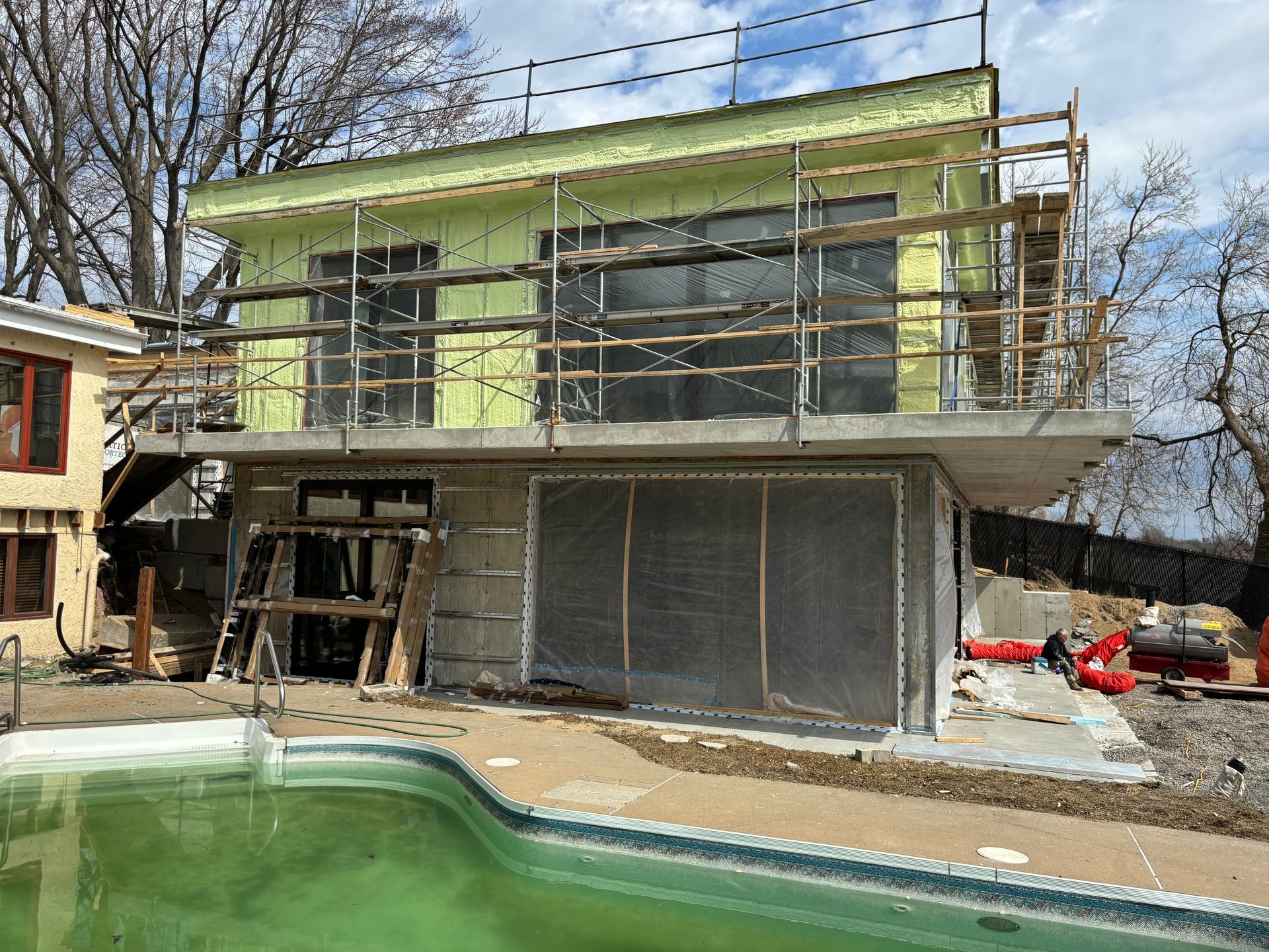 Bâtiment de deux étages en construction avec échafaudage à proximité d'une piscine verte.