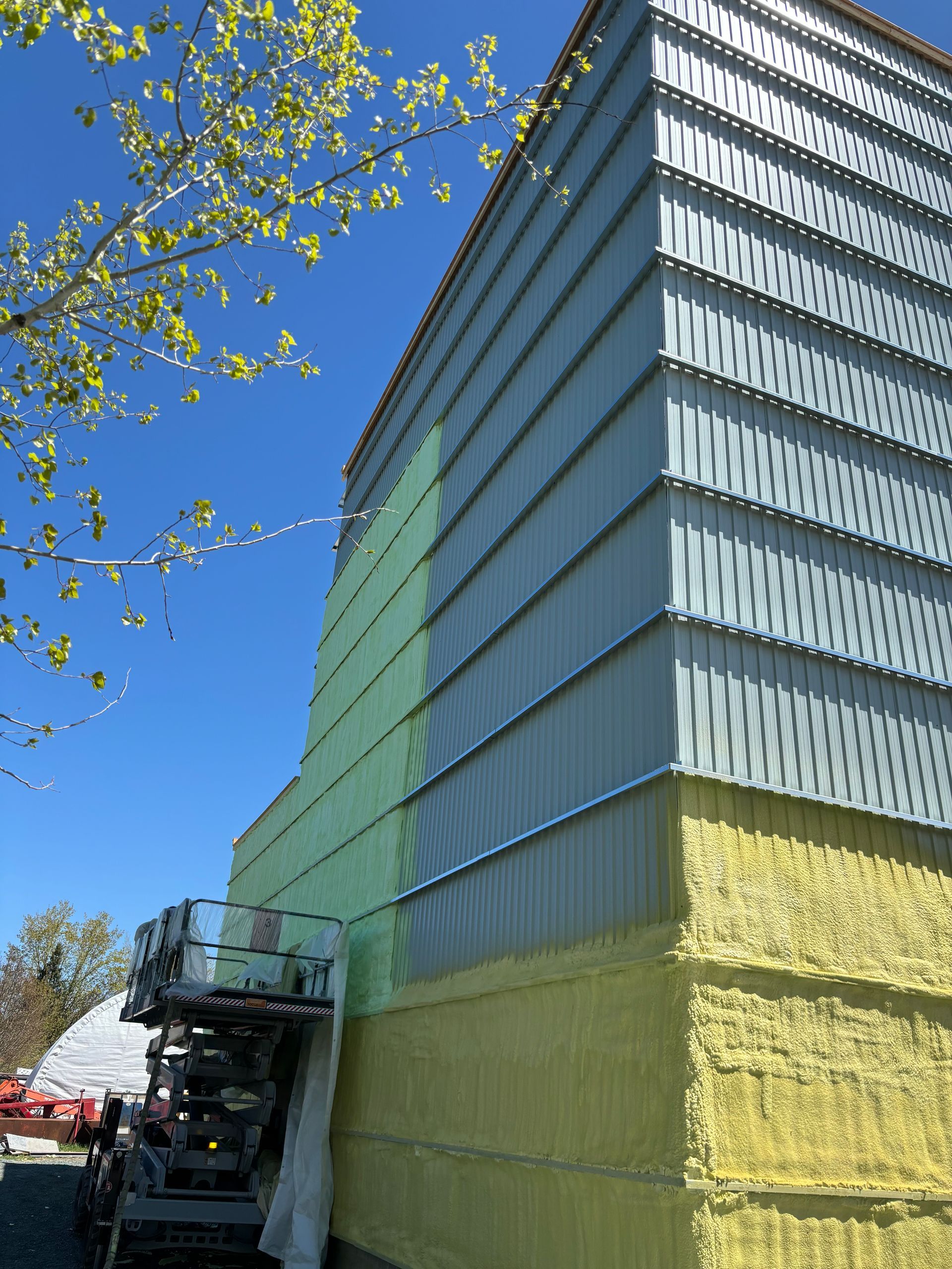 Chantier : Bâtiment avec bardage métallique, isolation jaune et ascenseur sur fond de ciel bleu.