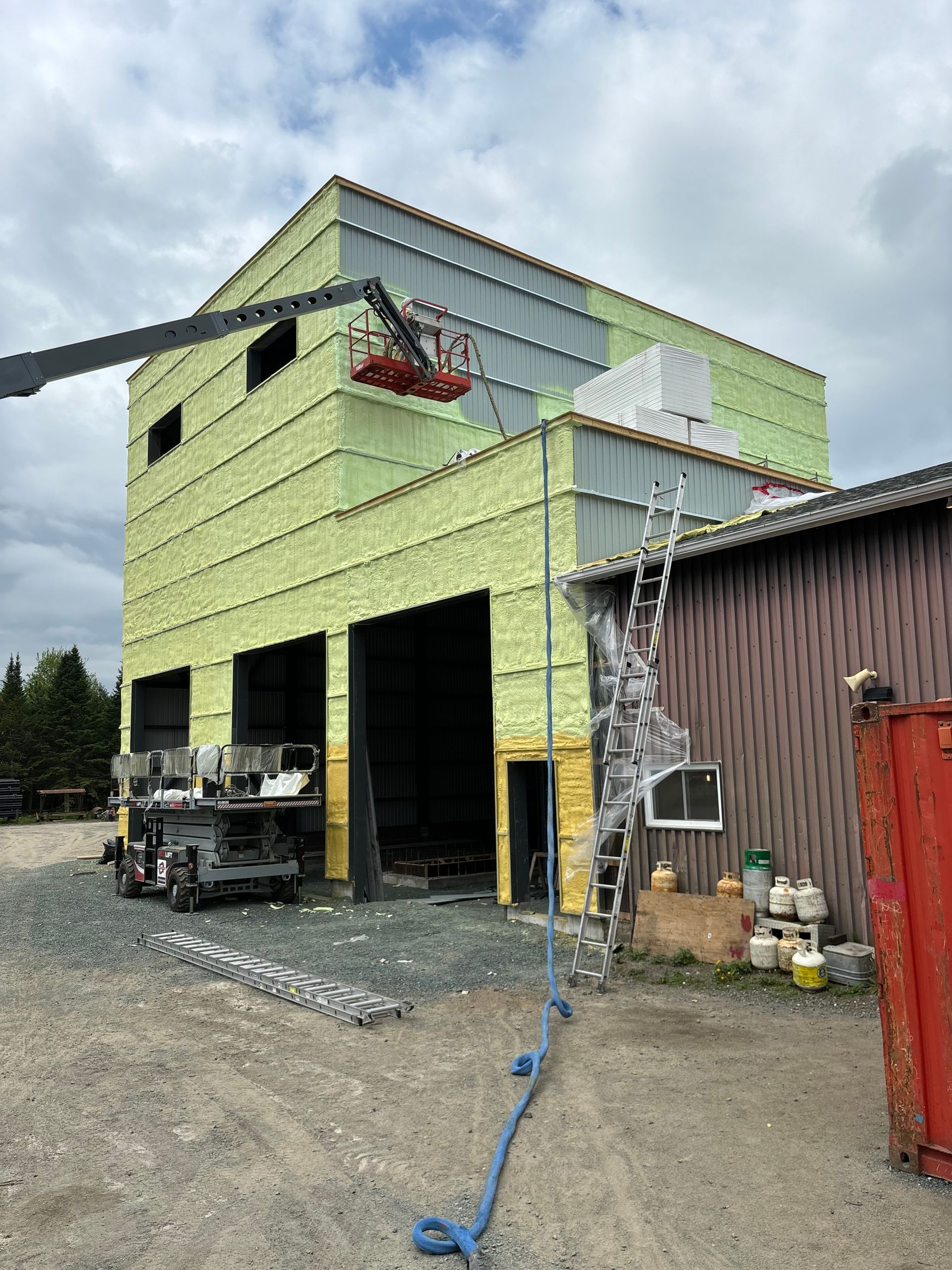 Chantier de construction avec un ascenseur en fonctionnement à proximité d'un bâtiment, qui dispose d'une isolation verte et d'une façade partiellement finie.