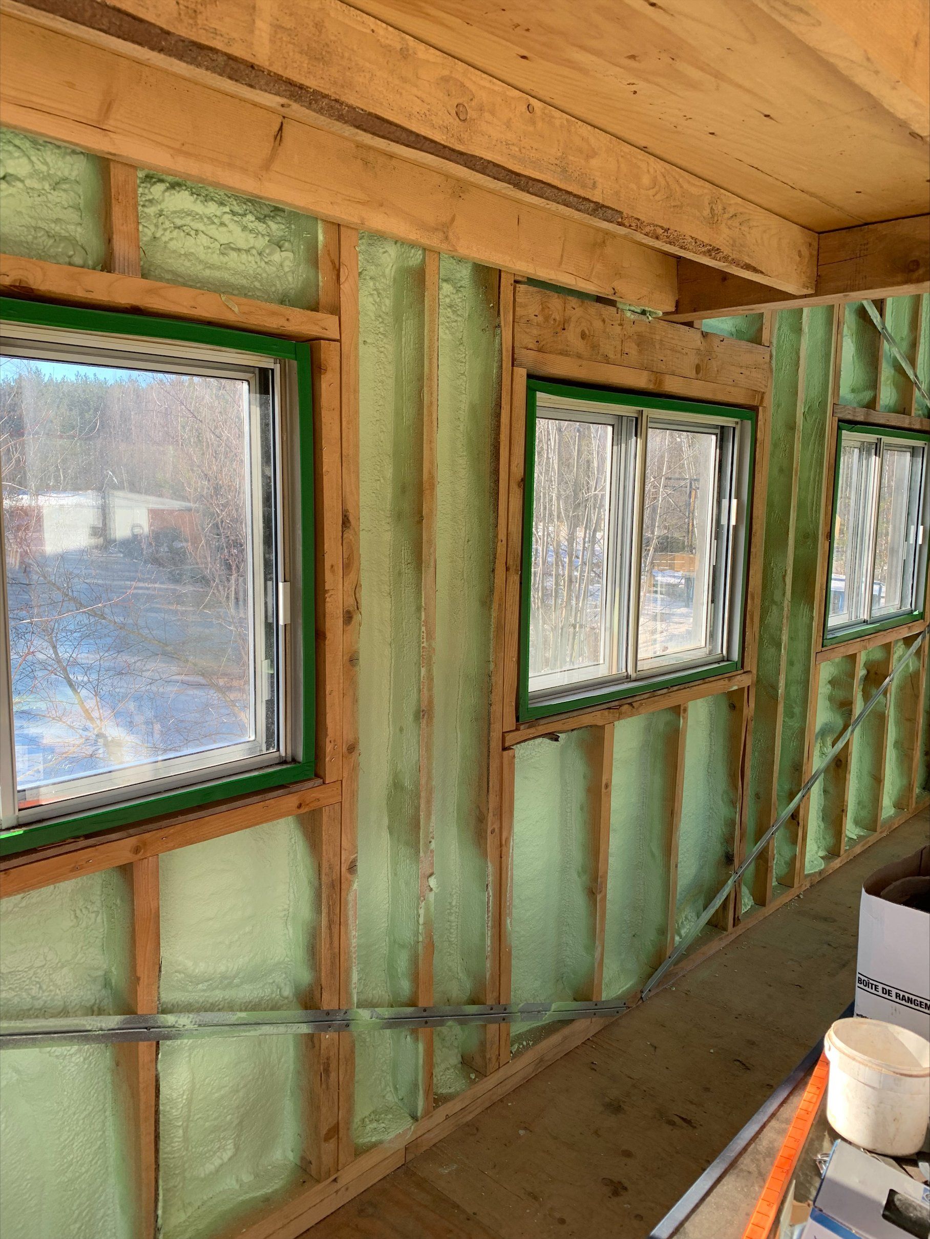 Vue intérieure d'un bâtiment en construction, montrant des fenêtres à encadrement vert et des murs isolés.