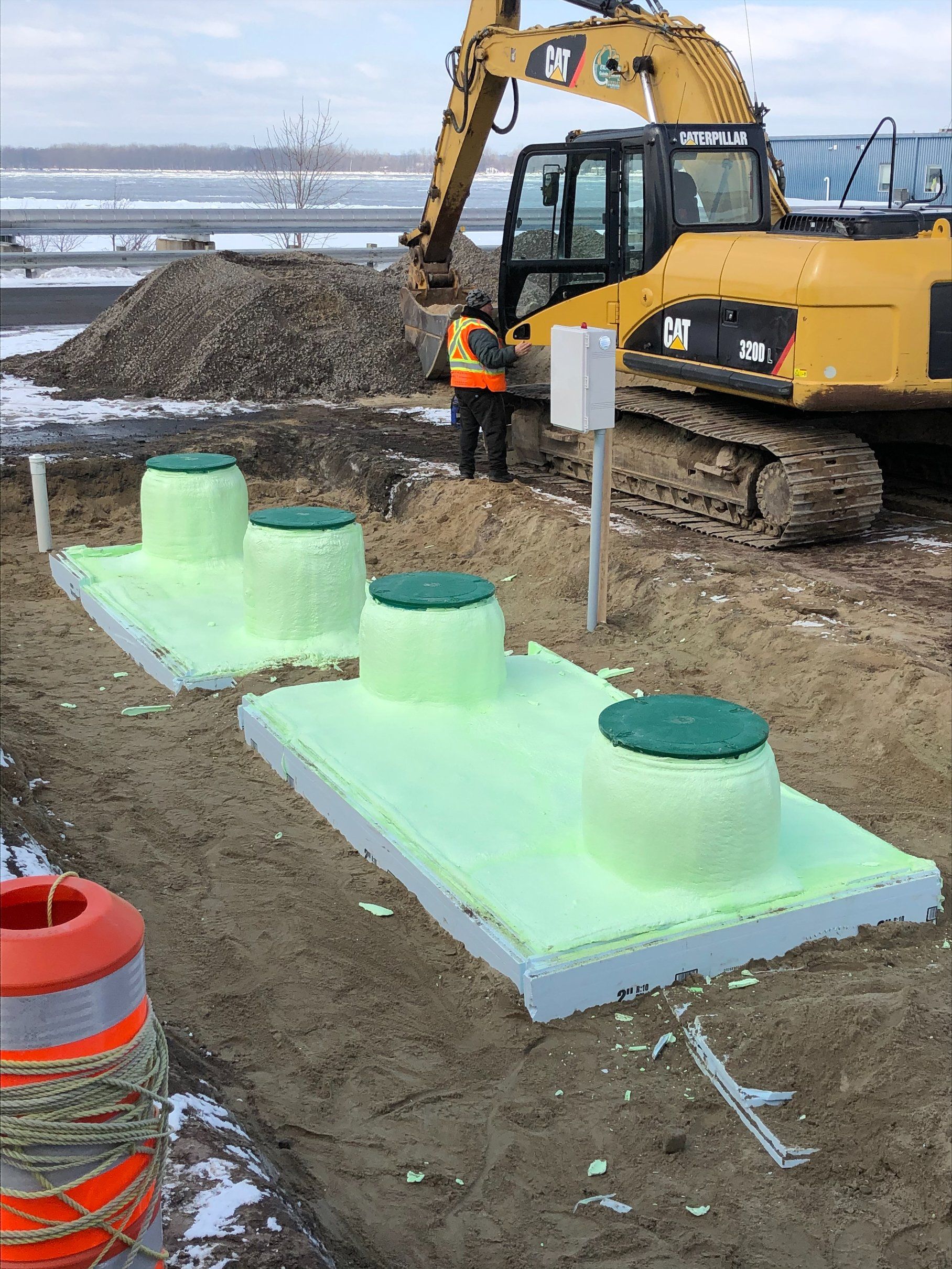 Trois fosses septiques préfabriquées en béton sont en construction près d'une excavatrice. Les fosses sont recouvertes d'un isolant vert.