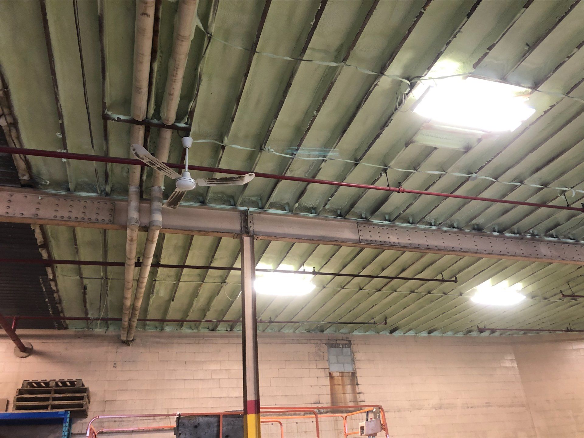 Plafond d'entrepôt avec panneaux métalliques isolés, tuyaux, poutres et luminaires encastrés.