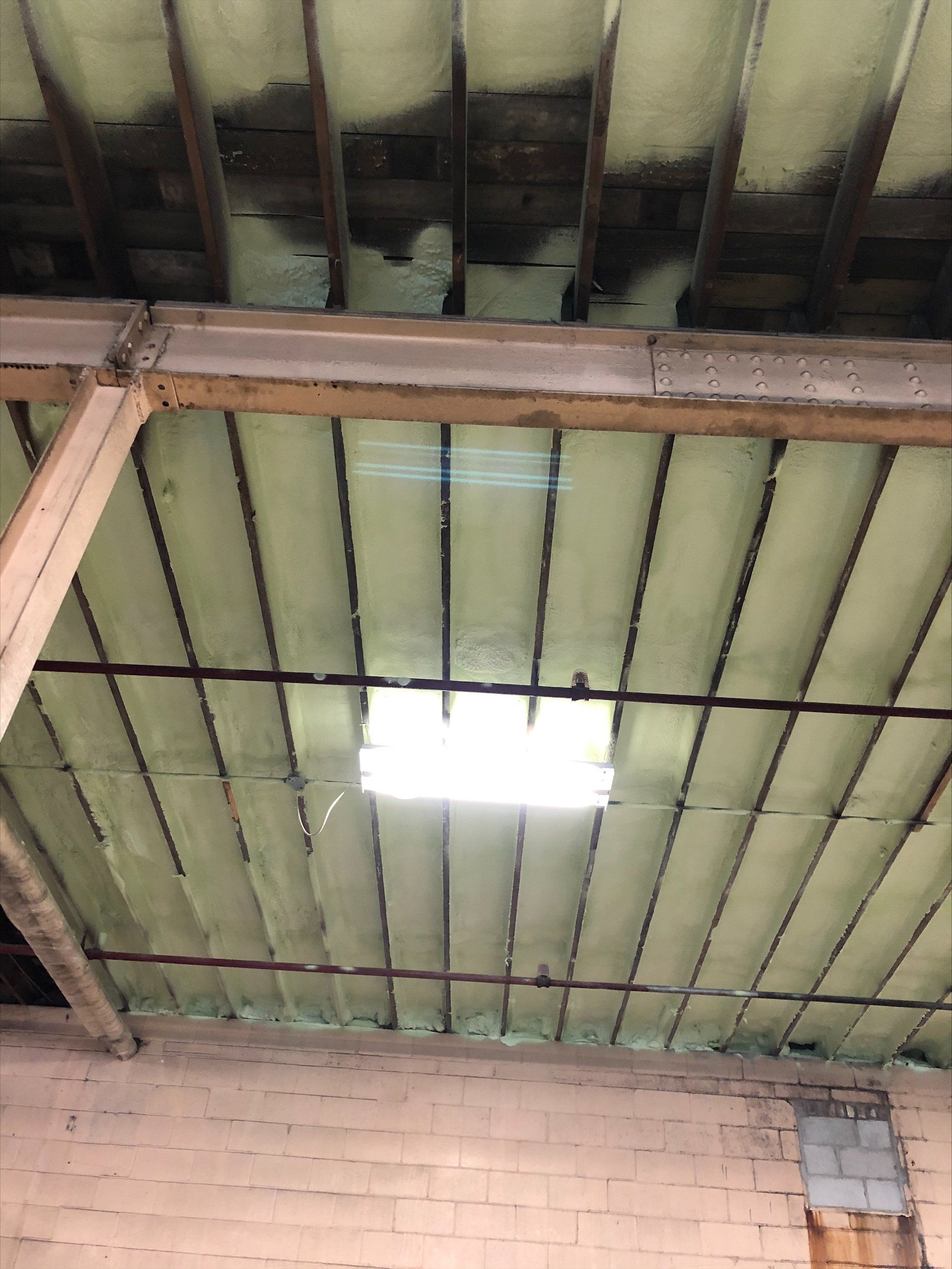 Plafond avec poutres apparentes, isolation vert clair et puits de lumière carré.