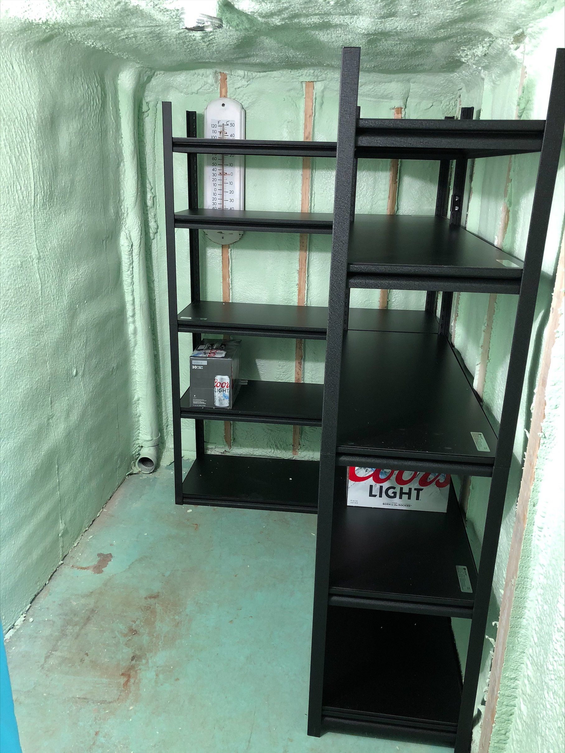 Étagère noire dans un petit débarras peint en vert ; un thermomètre est fixé au mur.