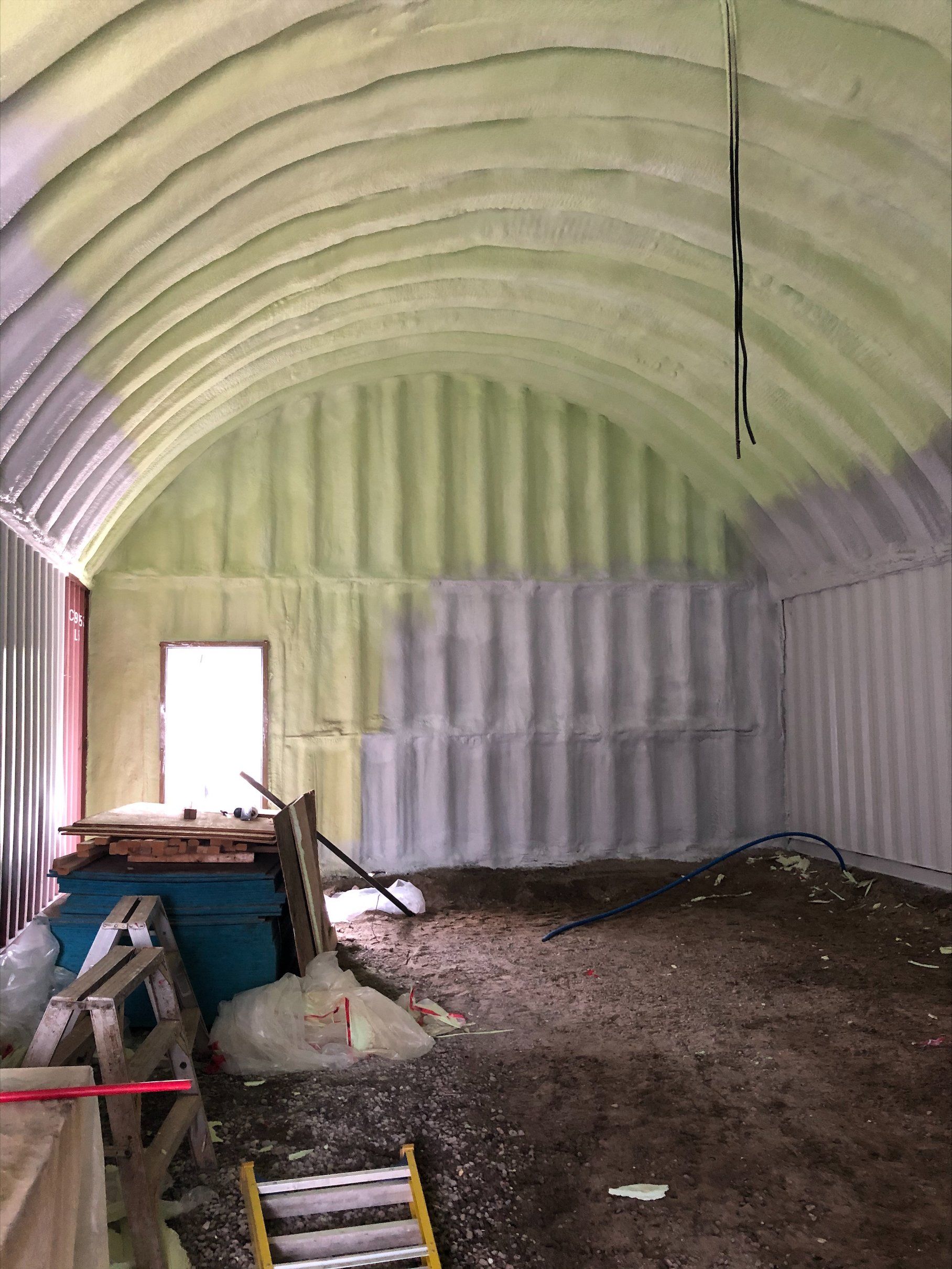 Intérieur d'un bâtiment avec des murs en tôle ondulée courbée, isolés avec de la mousse verte et grise.