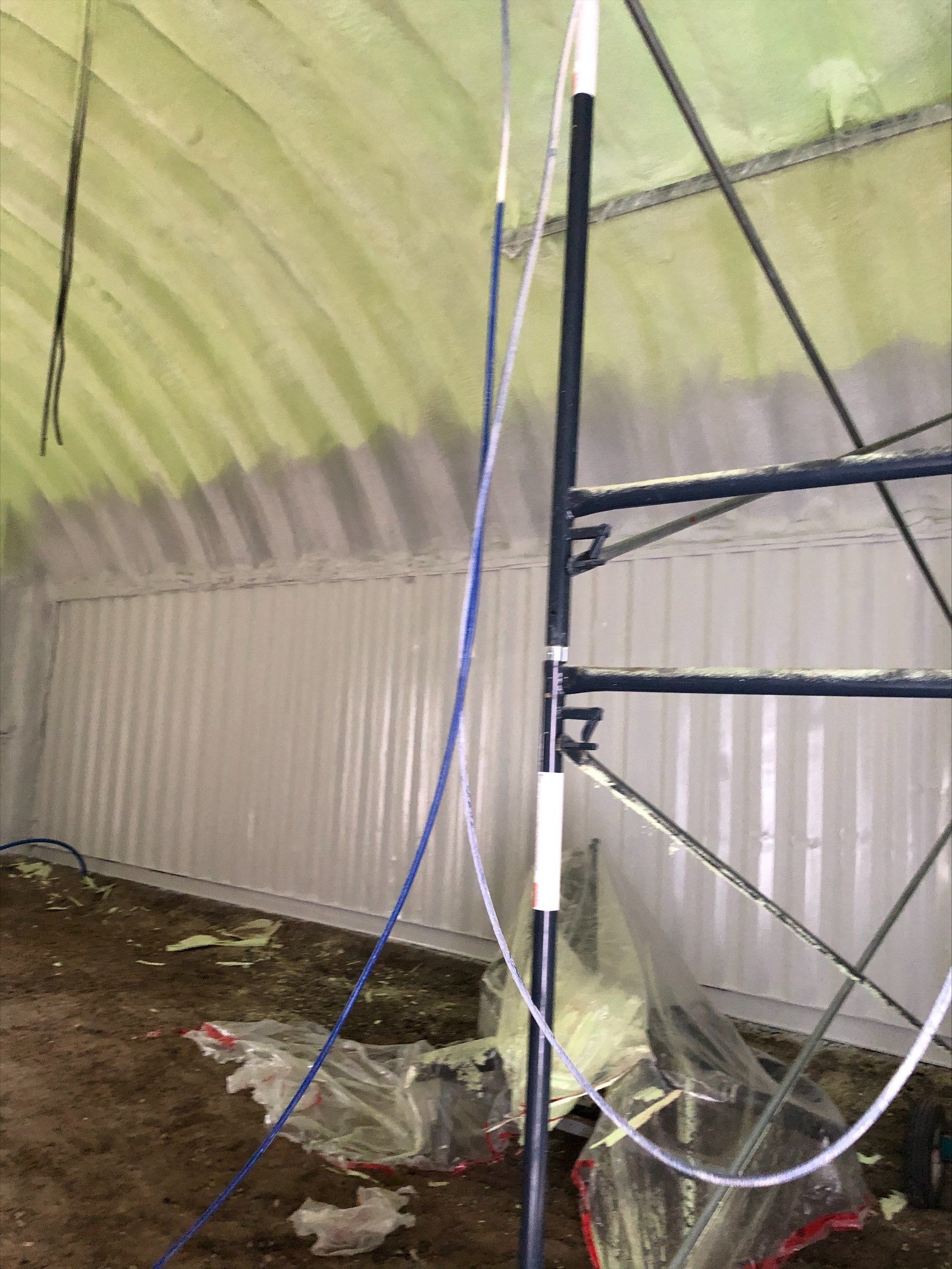 Intérieur d'un bâtiment en construction avec isolation en mousse pulvérisée, échafaudages et murs en tôle ondulée.