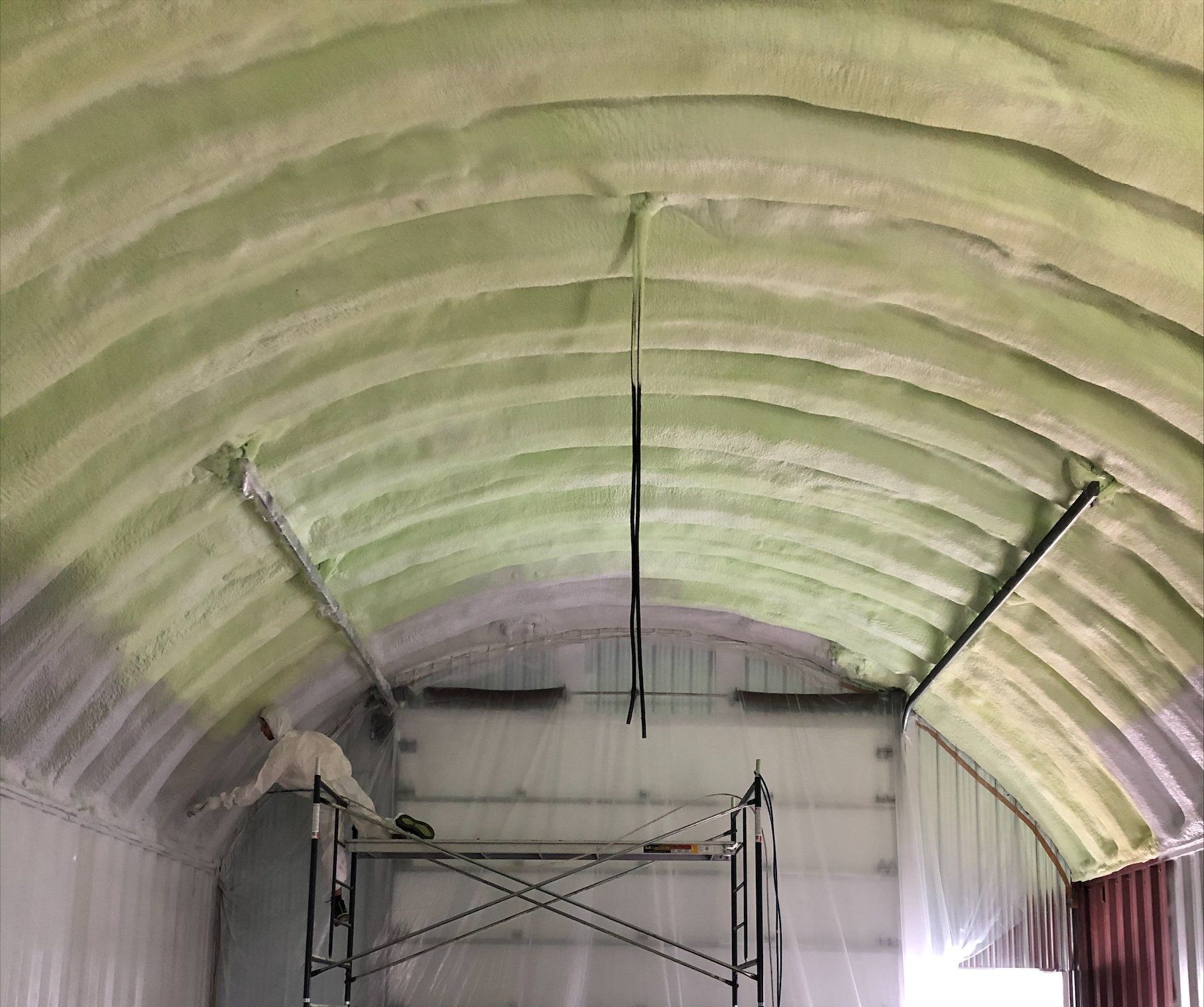 Isolation en mousse pulvérisée verte sur plafond voûté. Échafaudage en dessous, personne pulvérisant.