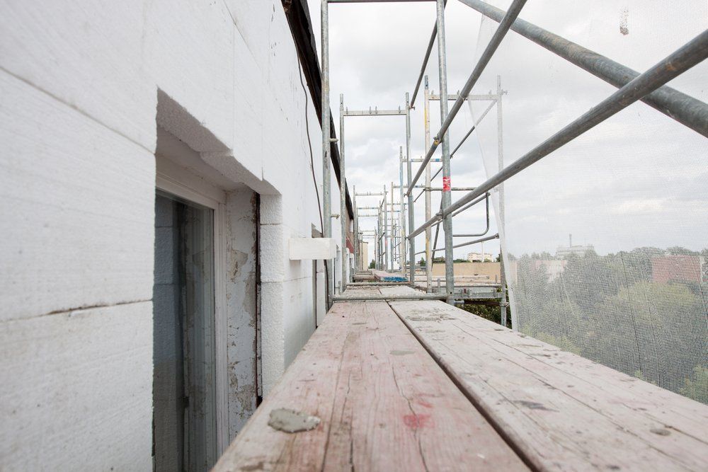 Plateforme d'échafaudage avec planches de bois, à côté d'un bâtiment blanc, ciel nuageux.