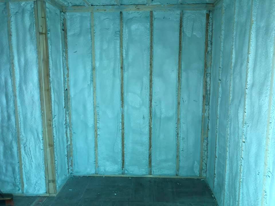 Vue intérieure d'une pièce avec des montants en bois et une isolation en mousse pulvérisée bleu clair sur les murs.