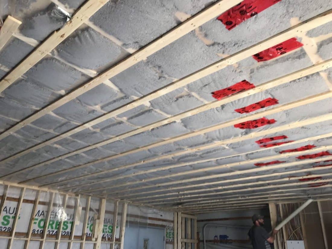Plafond en bois en construction avec isolation entre les poutres ; ouvrier en arrière-plan.