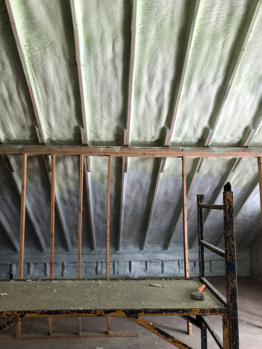 Une isolation en mousse projetée recouvre les chevrons et les murs d'un grenier. Un échafaudage métallique est visible au premier plan.
