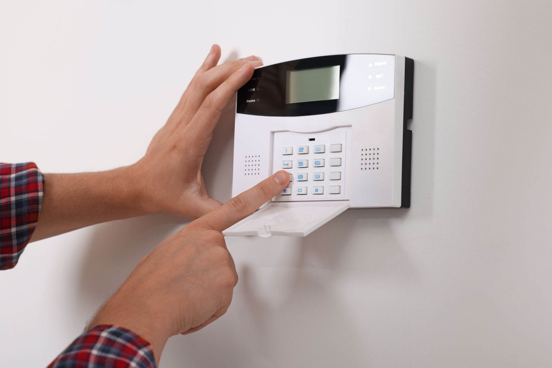 Hands entering a security code on a wall-mounted alarm keypad.
