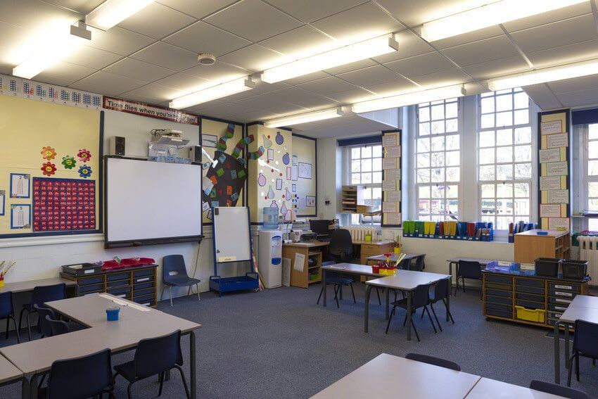 A horizontal image of an empty primary school classroom. The setting is typically British.