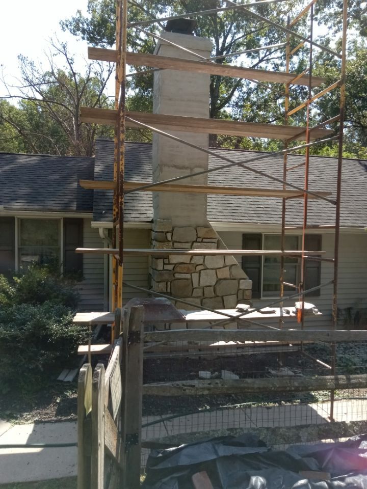 Stone fireplace under construction, surrounded by metal scaffolding outside a house.